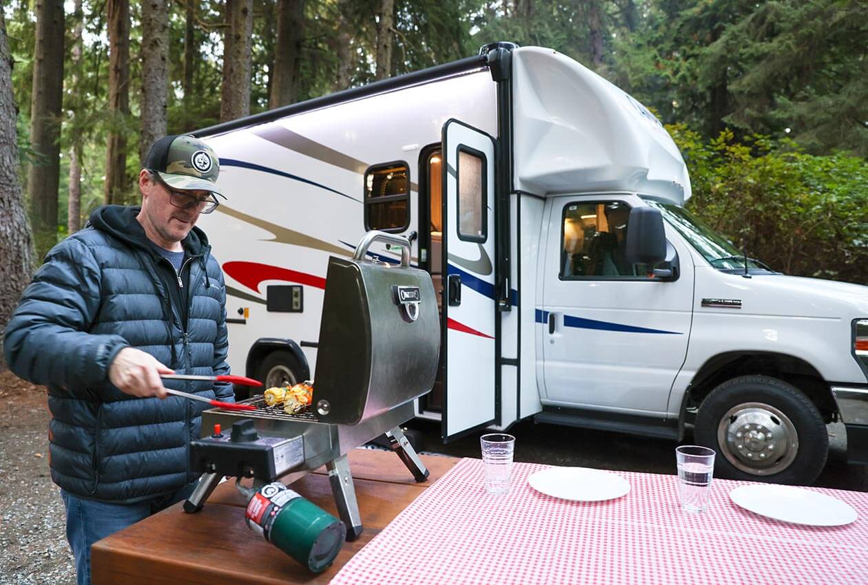 Two dogs and small child beside CanaDream Super Van Camper in campground